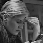 Mulher preocupada segurando celular esquentando e descarregando rápido com aviso de superaquecimento na tela